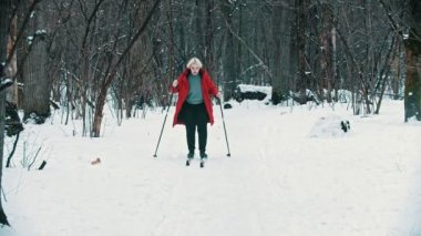 A young blonde woman in red down jacket walking on ski in the forest