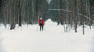 A young blonde woman in red down jacket skiing with an effort in the woods