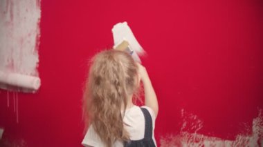 Girl is painting a red wall with a white brush