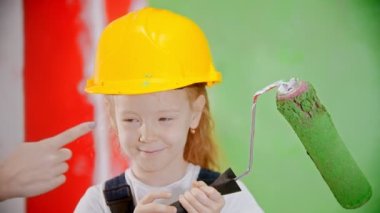 Little girl with a roller in her hands is standing looking at the camera and mom is smudging her nose with paint