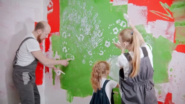 A család szórakozik és rajzol egy zöld falon, saját kezűleg fehér festékkel. — Stock videók