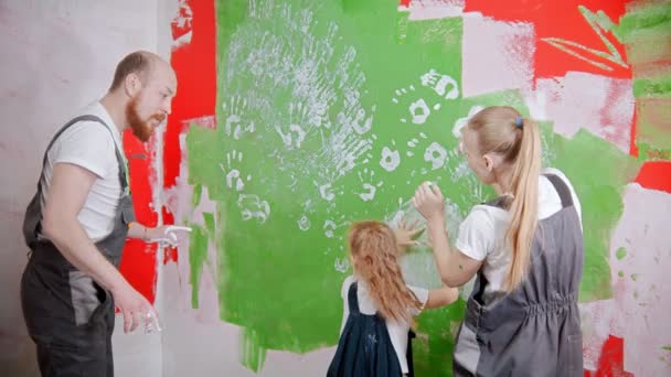 Family are drawing on a green wall with their own hands in white paint — ストック動画