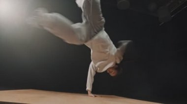 An athletic man dancer spinning around leaning on his hands on the wooden board