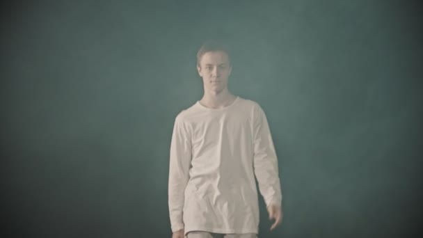 Молодой танцор, выходящий из дыма в темной студии и начинающий показывать элементы брейк-данса — стоковое видео