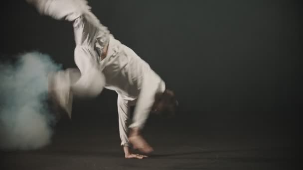 Fiatal férfi táncos bemutató breakdance elemek trükkök a sötét stúdióban — Stock videók