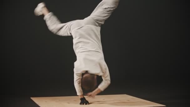 Молодий чоловік танцюрист кружляє навколо спираючись на руки на дерев'яній дошці — стокове відео