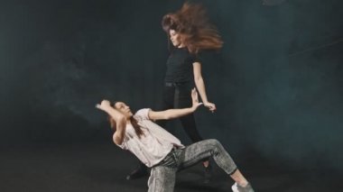 Two young women training their dancing in the dark studio