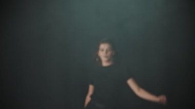 A young attractive woman with long hair walking out from the smoke in the studio