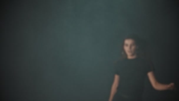 Молода приваблива жінка з довгим волоссям виходить з диму в студії і стоїть в позі — стокове відео