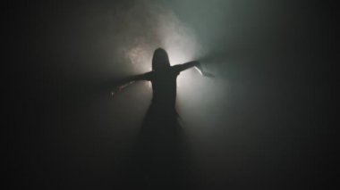 A silhouette of young attractive woman dancing on the background of bright lighting