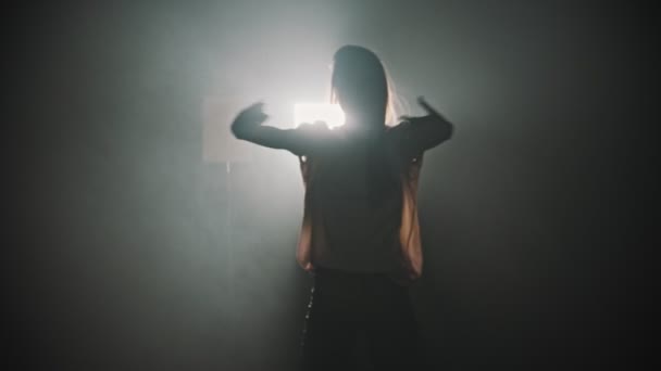 A silhouette of young woman dancing with her hands on the background of bright lighting — Stockvideo