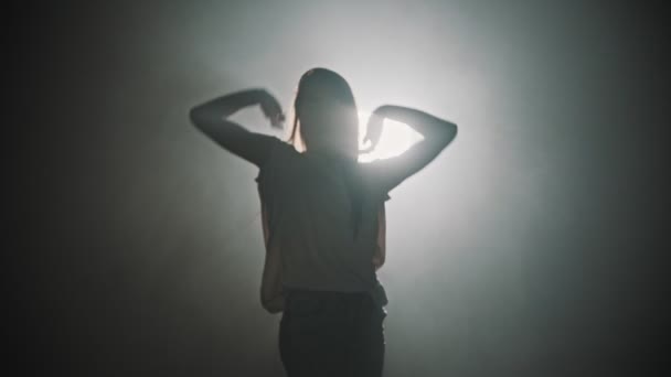 A silhouette of woman dancing with her hands on the background of bright lighting — 비디오