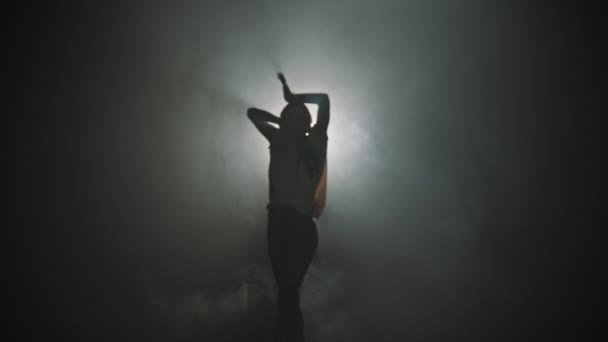 Силует молодої жінки, що танцює руками на тлі яскравого освітлення - виходить з темряви — стокове відео