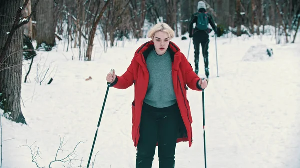 Blonde woman in red down jacket skiing with an effort in the forest — 스톡 사진