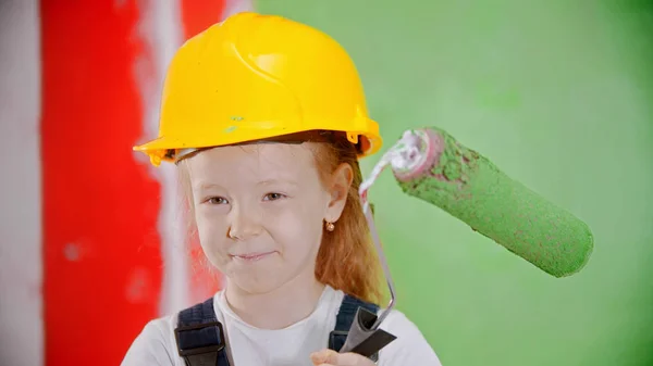 Счастливая маленькая девочка в шлеме держит ролик с краской и смотрит в камеру — стоковое фото