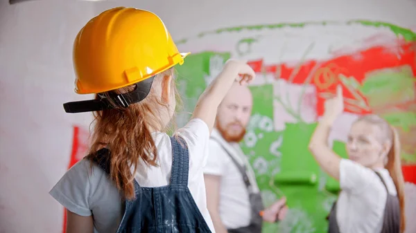 Een klein meisje in een helm wijst naar de muur - haar ouders staan naast de muur — Stockfoto