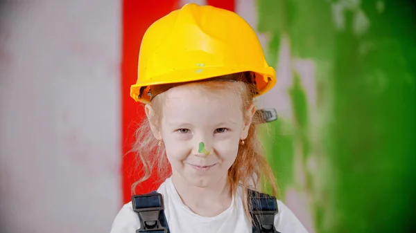 Glimlachend meisje in een helm houdt een verfroller vast en kijkt naar de camera - neus bedekt met groene verf — Stockfoto