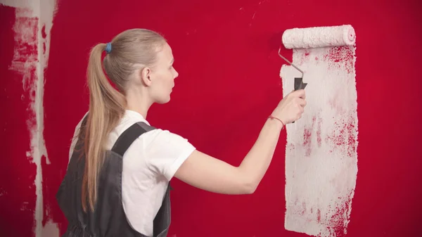 女性は白いローラーで赤い壁を描いています — ストック写真