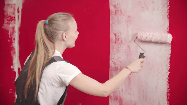 Jonge vrouw schildert een rode muur met een witte roller — Stockfoto