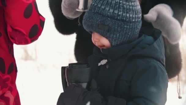Маленький хлопчик п'є чай з термокубку в оточенні своєї сім'ї — стокове відео