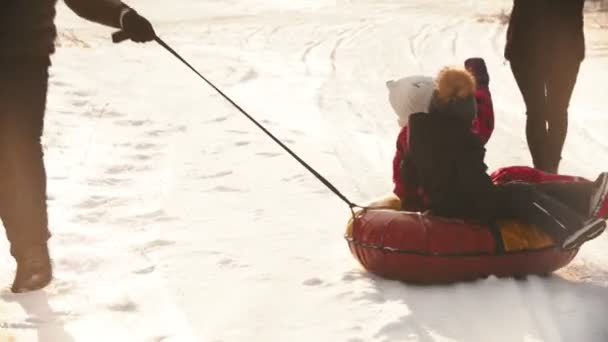 A man father rolls his kids on the inflatable sled around himself — 图库视频影像