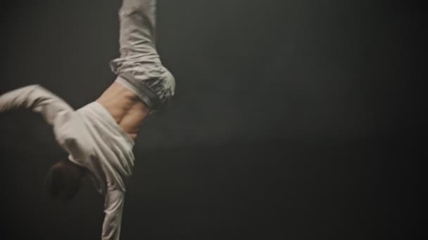 Young sportive man training his breakdancing tricks in the dark studio — Stock Video