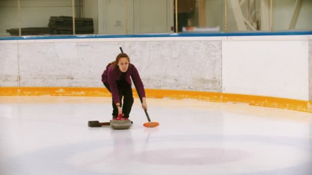 Curling - a young woman pushes off in the ice field with a granite stone — Stock Video