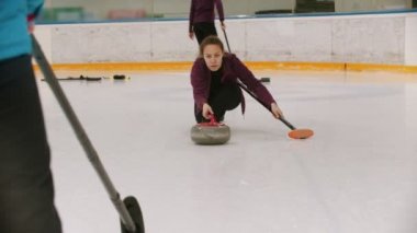 Curling - a woman skating on the ice field with a granite stone and releasing it