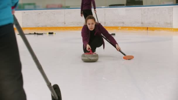 Curling - uma mulher patinando no campo de gelo com uma pedra de granito e liberando-o — Vídeo de Stock