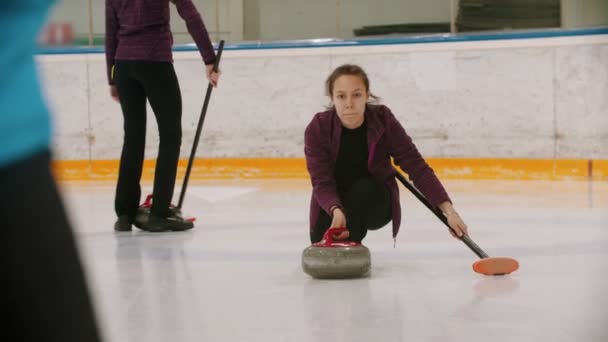 Curling - una mujer patinando en el campo de hielo y liderando una piedra de granito — Vídeo de stock