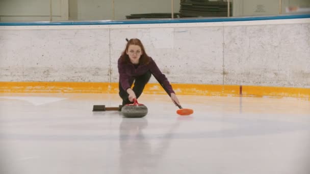 Curling - kobieta w okularach jeżdżąca na łyżwach i wiodąca główna granitowa skała na polu lodowym — Wideo stockowe