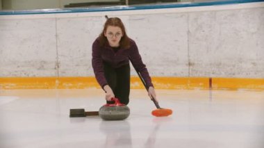 Curling training - a woman in glasses skating and leading main granite stone on the ice field