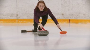 Curling - a woman in glasses skating on the ice field and leading a granite stone to the certain point holding a brush