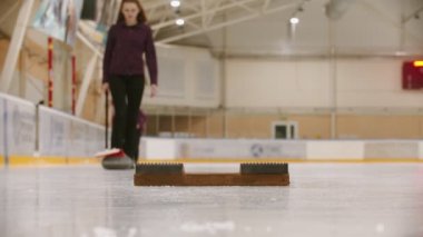 Curling training - a woman pushes the granite stone using a brush - skating to the stand