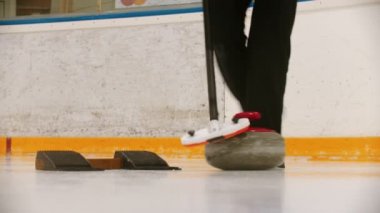 Curling - a womans hand pushes off from the stand with granite stone