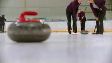 Curling training - leading granite stone on the ice - two women rubbing the ice before the stone