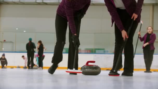 Curling training indoors - leading granite stone on the ice - two women rubbing the ice before the stone — 图库视频影像