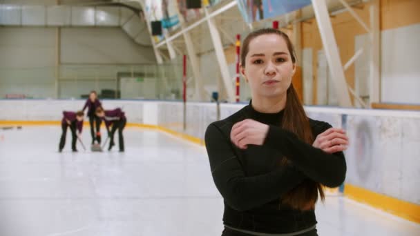 Curling training - de rechter die op de ijsbaan staat en in de camera kijkt - haar studenten die curling spelen op de achtergrond — Stockvideo