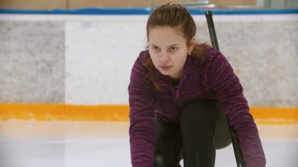 Curling training op de ijsbaan - een jonge vrouw duwt van de tribune met een steen — Stockvideo