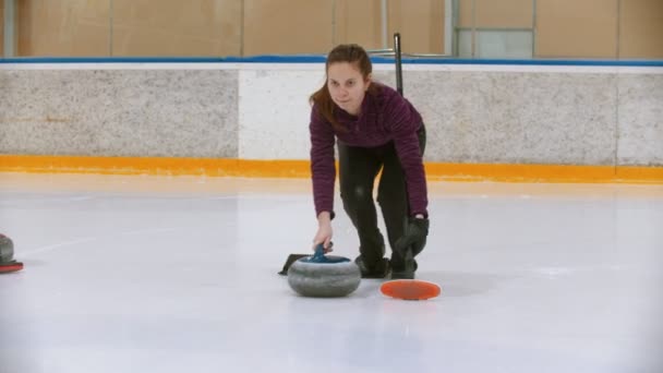 Trening curlingu na lodowisku - młoda kobieta odpycha się od stojaka z ukąszeniem kamienia — Wideo stockowe