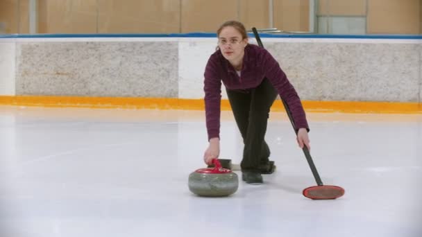 Trening curlingu - młoda kobieta odpycha się od podstawki z ukąszeniem kamienia — Wideo stockowe