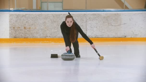 Curling školení - mladá žena s dlouhými vlasy tlačí z tribuny - vede kámen kousnutí — Stock video