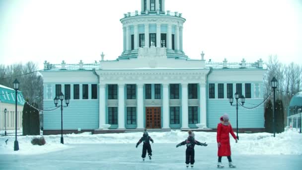 Genç bir anne ve iki çocuk bir binanın arka planında halka açık buz pateni pistinde paten kayıyor. — Stok video