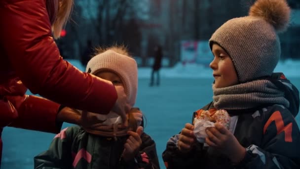 Молодая женщина кладет пончик в бумагу для своего сына и дочери — стоковое видео