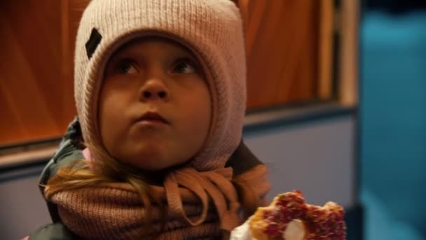 En liten flicka i vinterkläder äter munk utomhus — Stockvideo