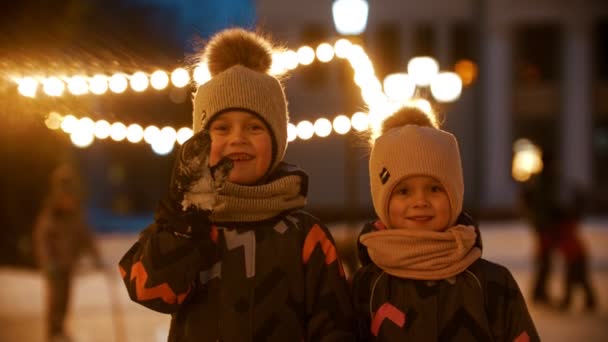 Dvě malé děti stojící na veřejném kluzišti a dívající se do kamery — Stock video