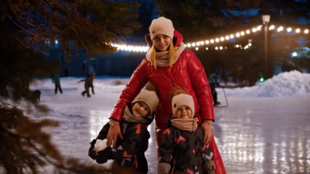 Genç bir anne ve iki çocuklu bir aile donanımlı buz pateni sahasında duruyor ve elleriyle el sallıyorlar. — Stok video