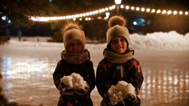 İki küçük çocuk halka açık buz pistinde durur ve havaya kar fırlatırlar. — Stok video