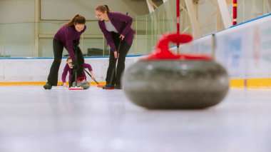 Curling training - leading granite stone on the ice - two women rubbing the ice before the stone to move others hostile stone from the point