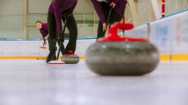 Kıvrımlı - buz üzerinde lider granit taş - iki kadın diğer düşmanca taşları hareket ettirmek için buzu taştan önce ovuyor